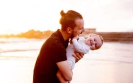 man in black t shirt carrying baby in white onesie