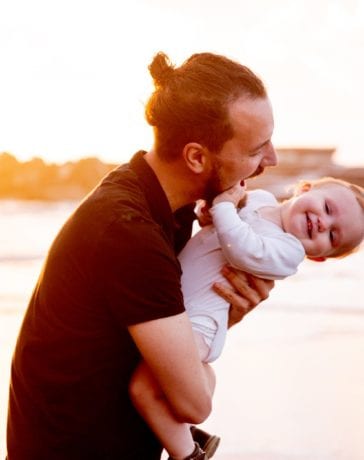 man in black t shirt carrying baby in white onesie